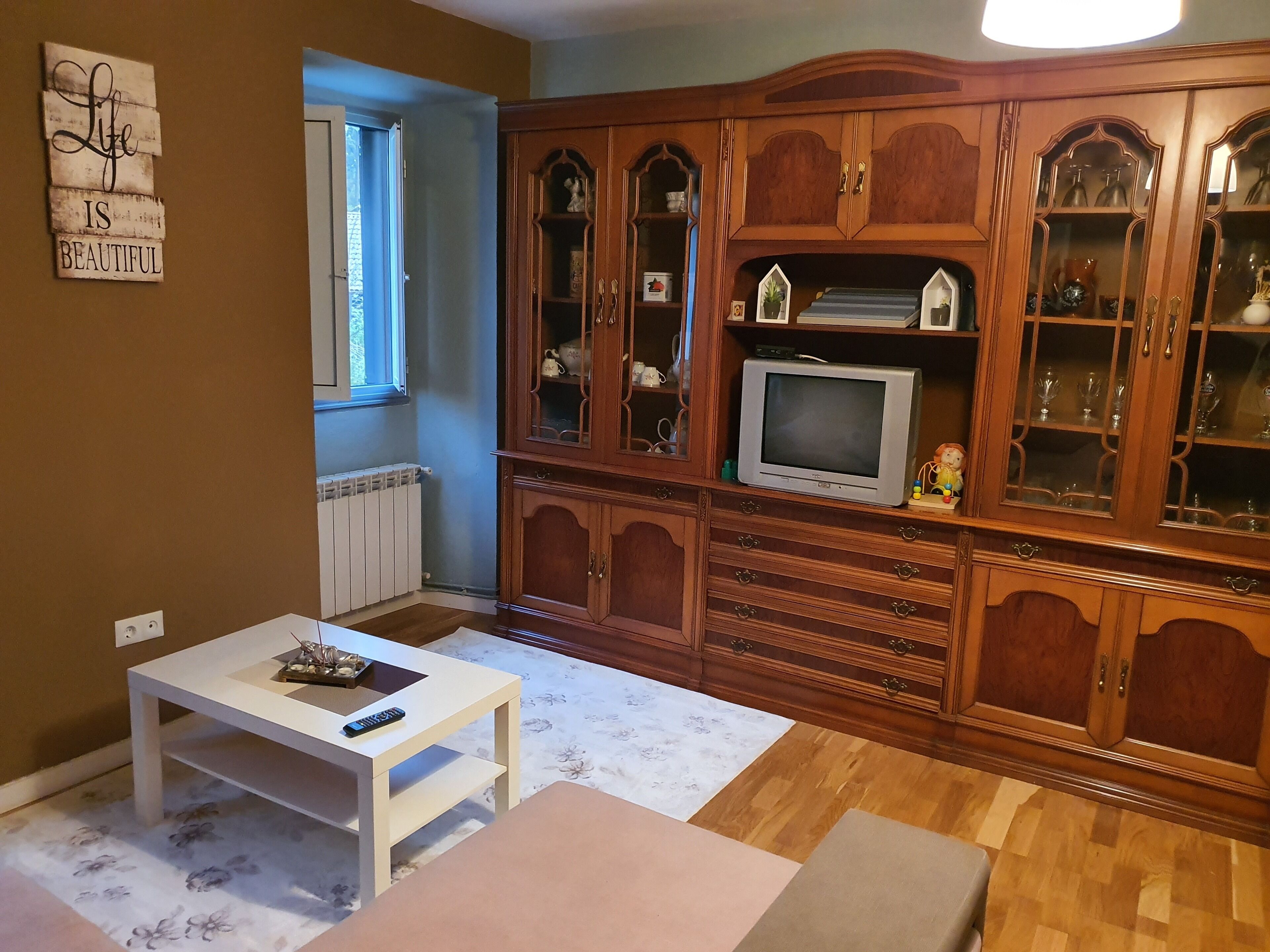 A living room with a wooden cabinet, a television, and a white table.