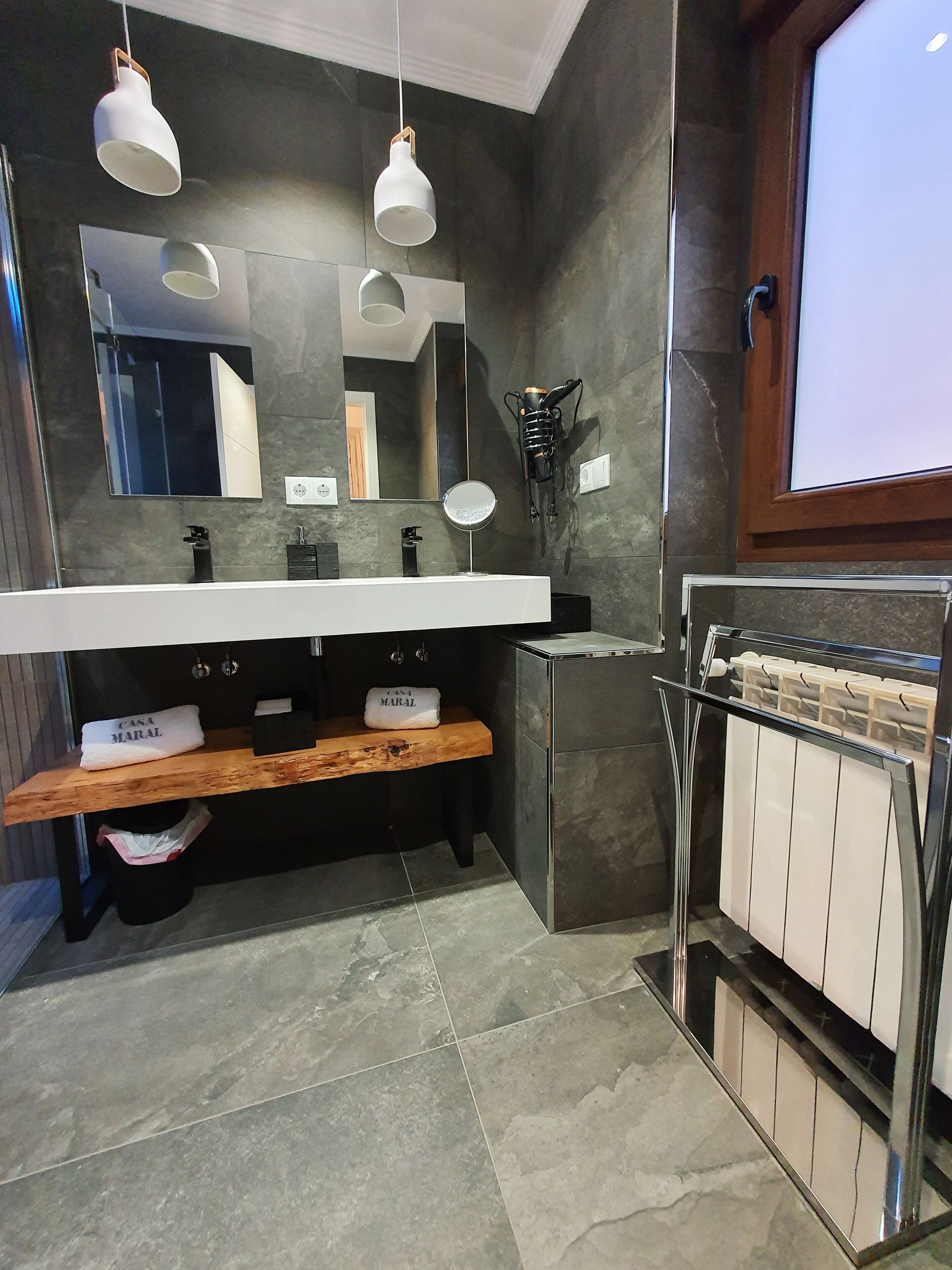 Un baño moderno con un espejo grande, dos lámparas colgantes, un perchero y un toallero.