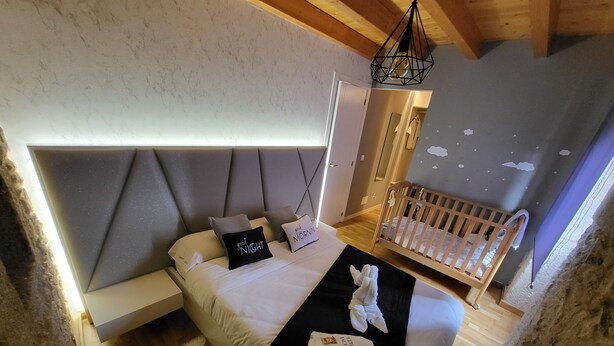 Een slaapkamer met een bed, nachtkastje, ledikant en een hanglamp.