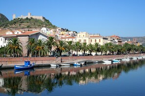 A coastal town with a historic castle on a hill, a row of colorful buildings, and boats docked along the waterfront.