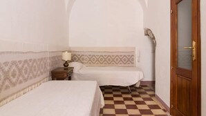Habitació d'hotel amb dos llits, un sòl amb quadres, una porta de fusta i una paret amb motius.
