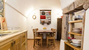 Cuina amb taula de menjador, cadires, rellotge i prestatges plens de vaixelles.