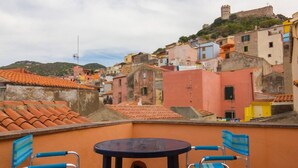 Terrassa amb dues cadires blaves i una taula rodona, amb vista a una ciutat colorida als vessants d'una muntanya, amb edificis històrics i un castell al cim.