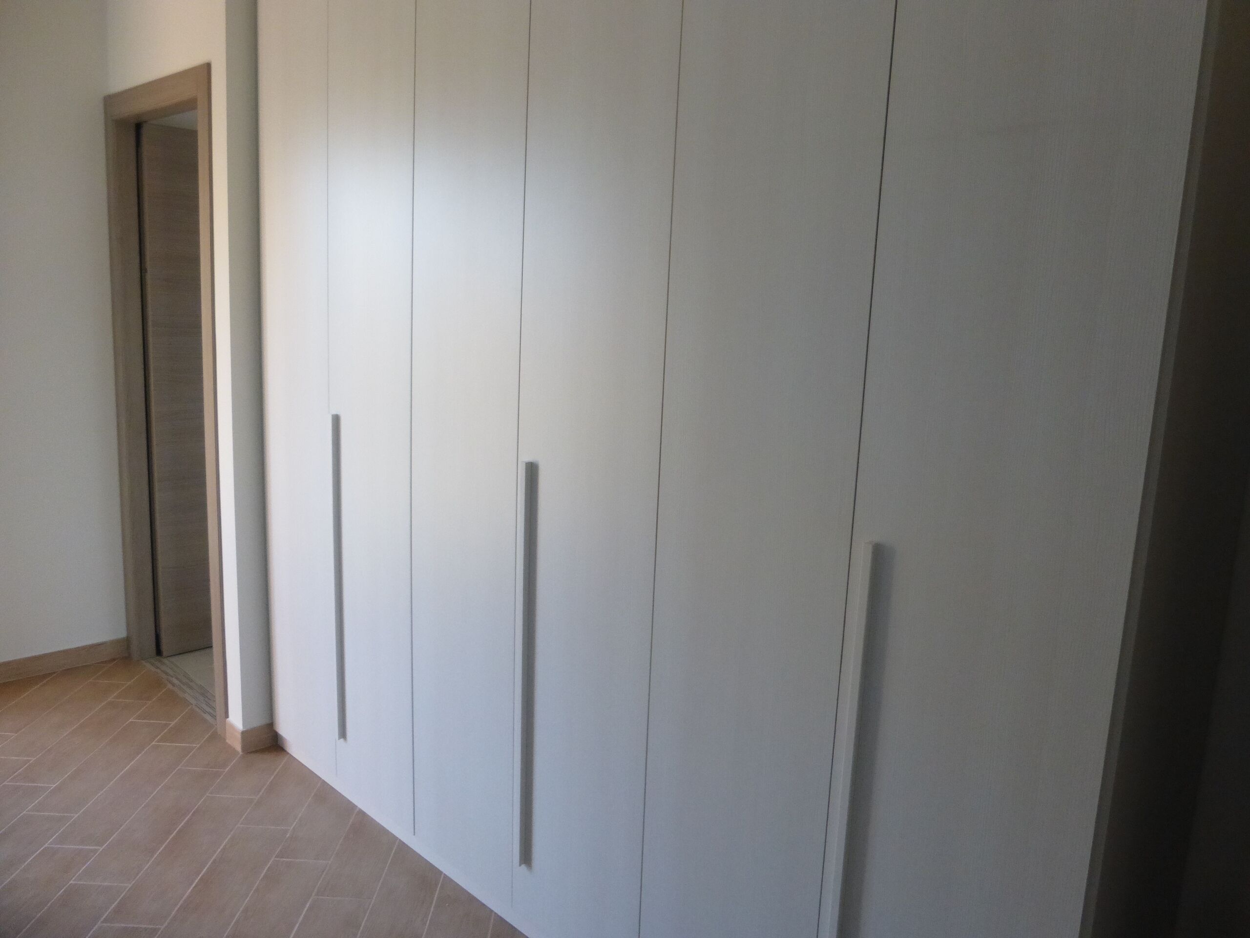 A hallway with a plain white wall and a door at the end.