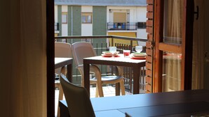 Un balcon ouvert, agrémenté de meubles en osier, une table dressée pour le repas et une vue sur un immeuble doté de balcons.