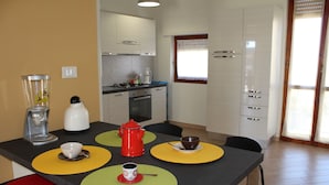 Une cuisine compacte avec un coin repas, équipée d’une machine à café, d’une bouilloire et d’une théière rouge.