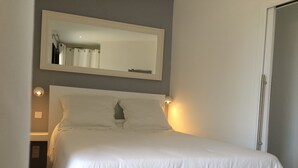 A neatly made bed in a room with a large mirror above it, a bedside lamp, and a door to the right.