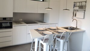 A modern kitchen with white cabinetry, a built-in oven, a stainless steel sink, and a bar area with stools.