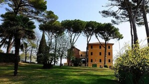 A building with a flat roof and multiple windows, surrounded by a grassy area with trees. - Hotel Sacro Cuore (Perugia)
