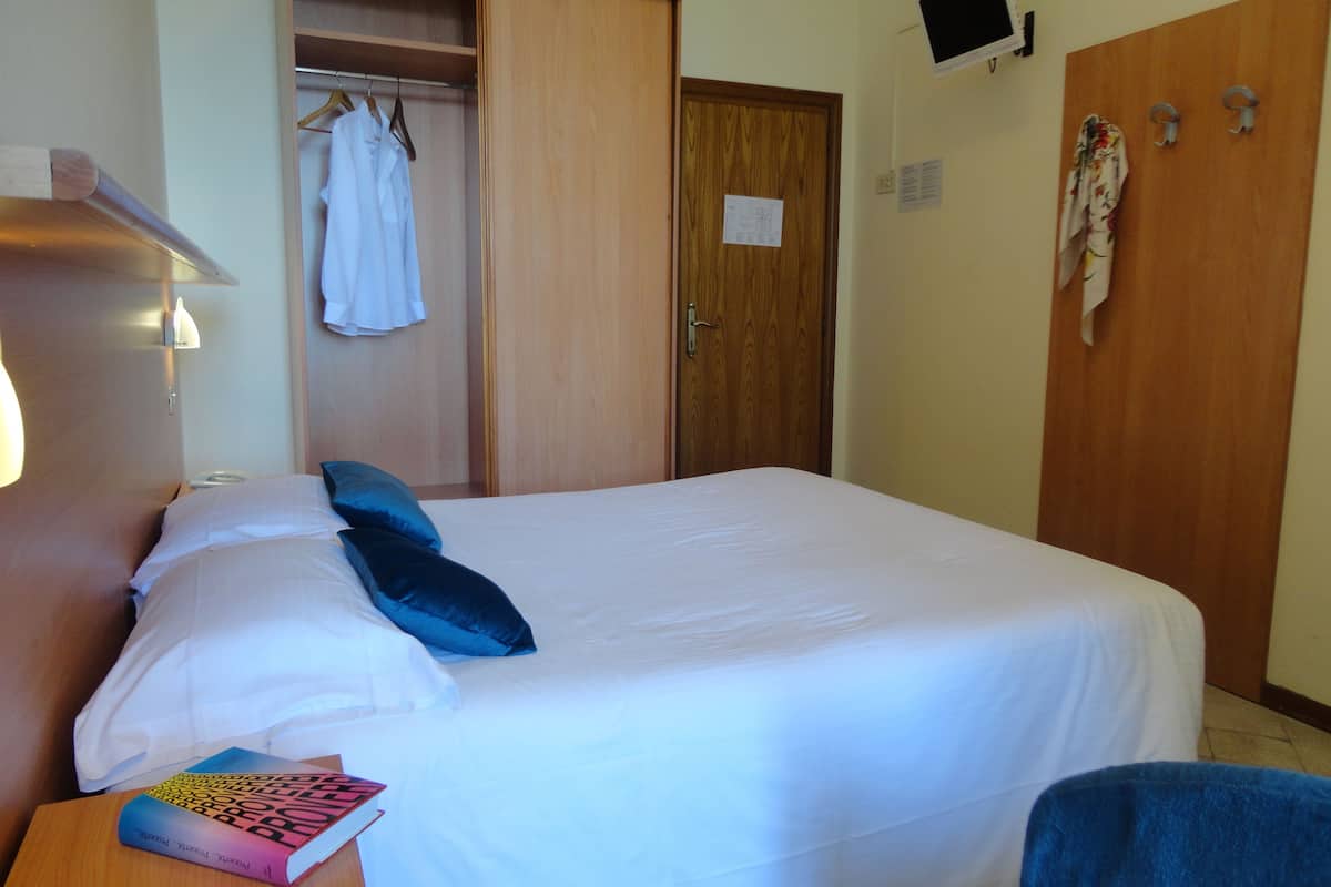 A hotel room with a bed, a bedside table with a book, a wardrobe, and a television mounted on the wall.