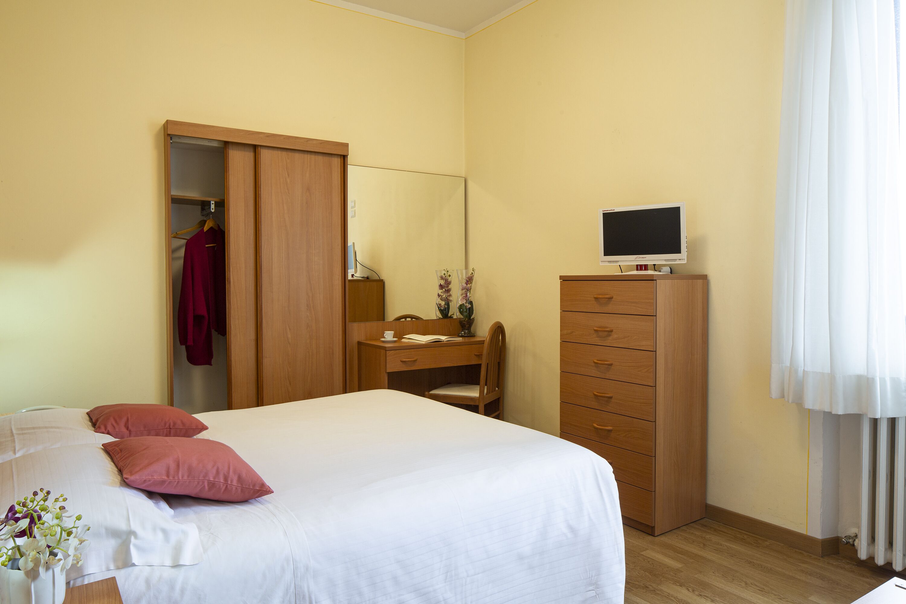 Una habitación de hotel con cama, escritorio, silla, armario y televisor.