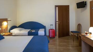 Habitación de hotel con dos camas, un escritorio, una silla, un televisor y una maleta.