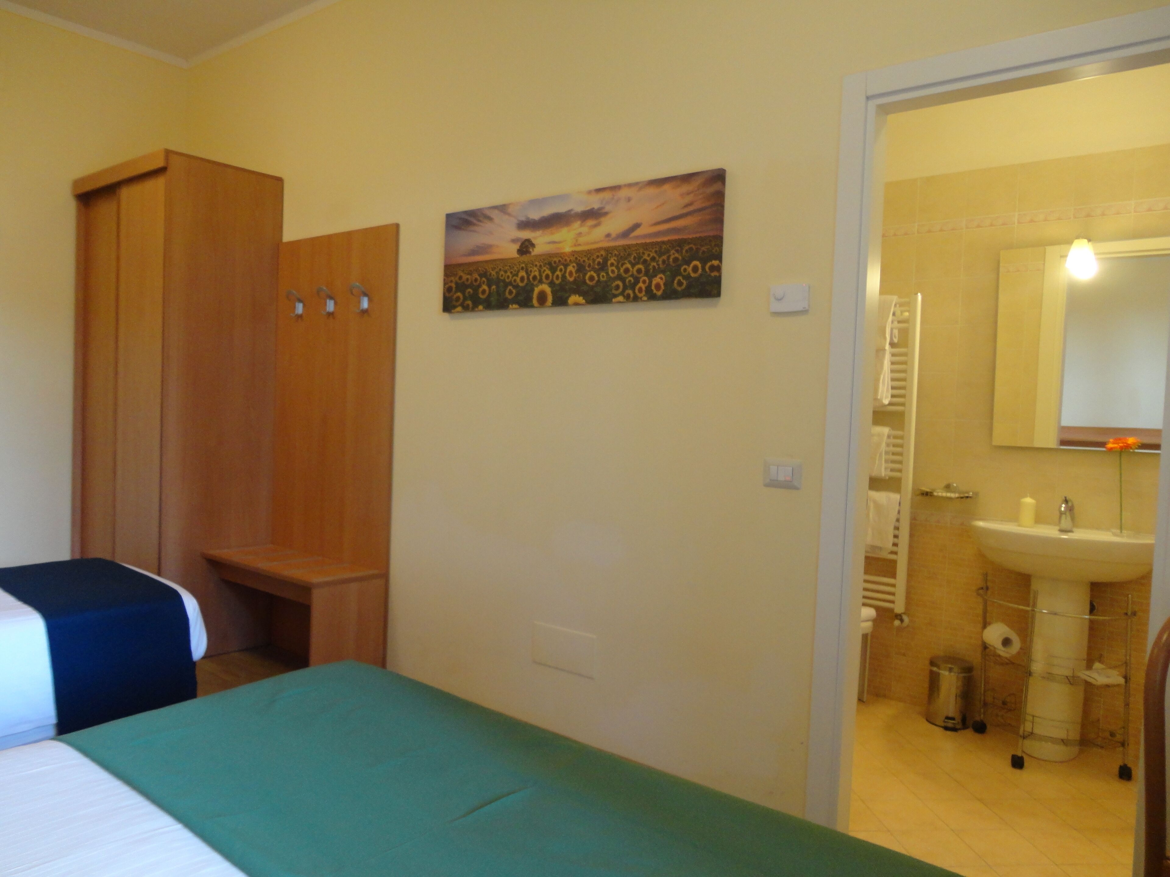 Un dormitorio con cama, armario, un cuadro, y baño con lavamanos y espejo.