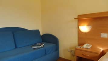 Un sofá azul con un libro y gafas, una mesita de noche con un teléfono, y una lámpara de pared.