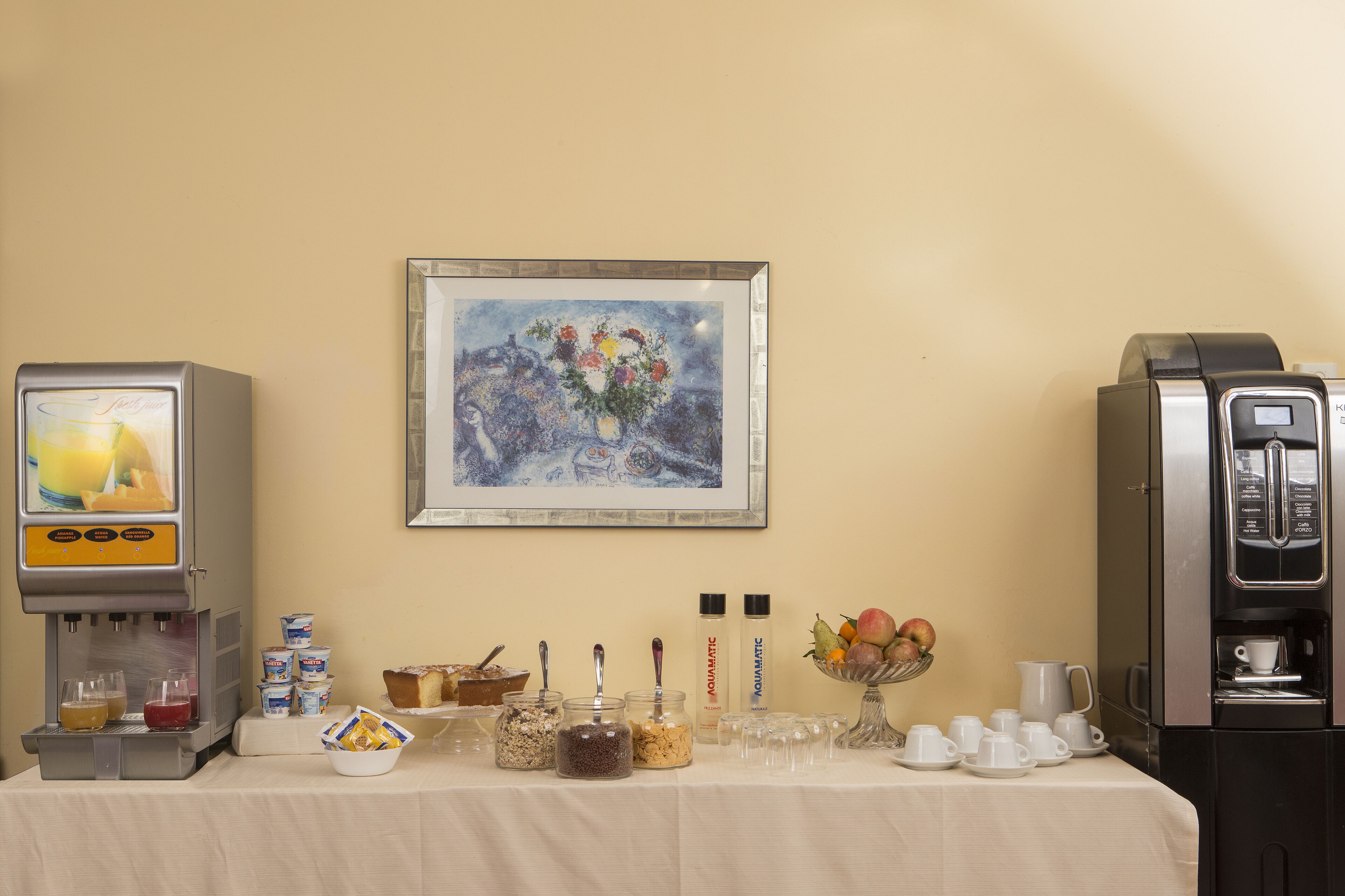 A breakfast setup with a coffee machine, juice dispenser, and various food items on a table.