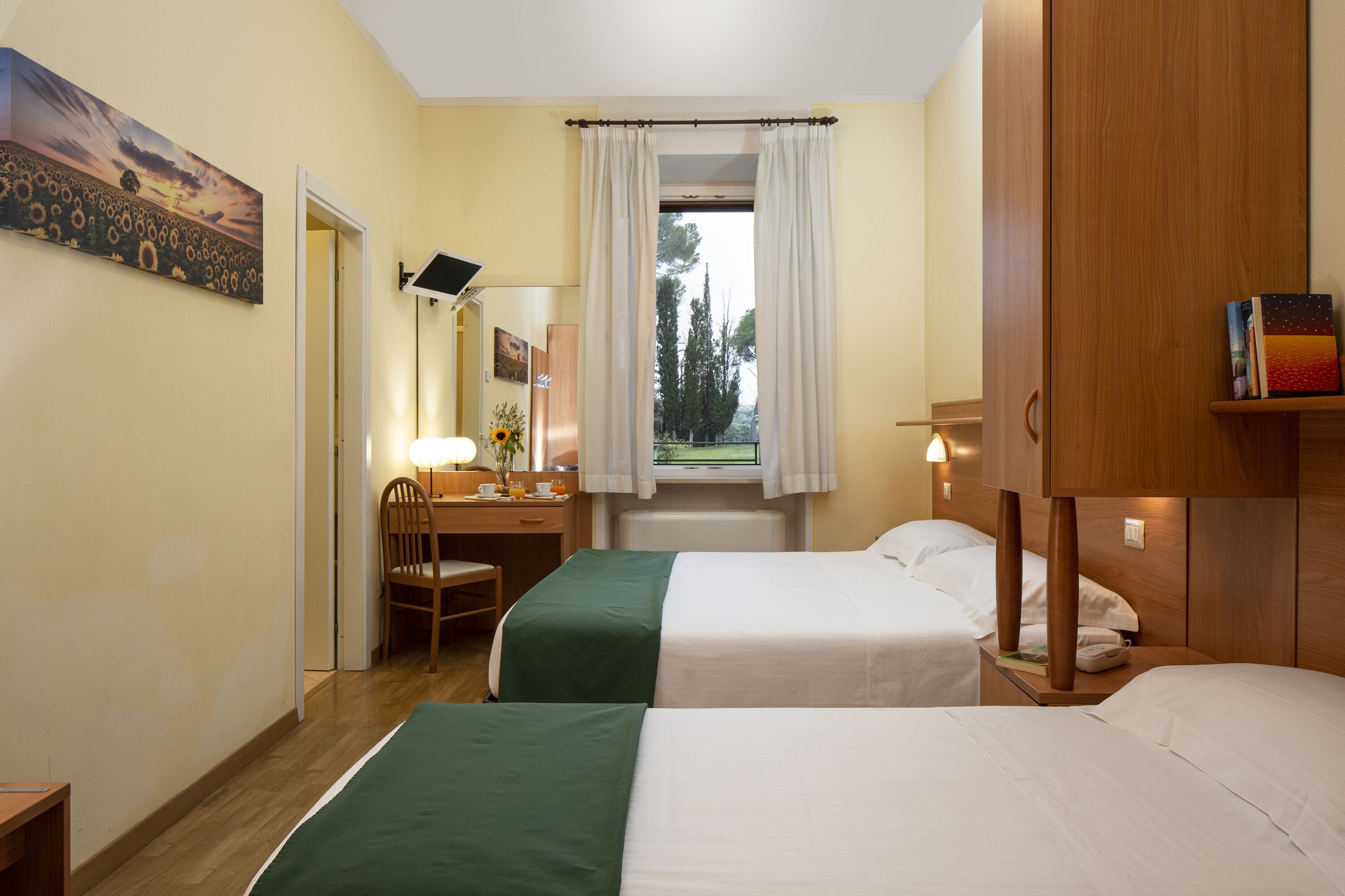 Une chambre d’hôtel avec deux lits, un bureau avec une chaise, une fenêtre avec des rideaux et un tableau au mur.