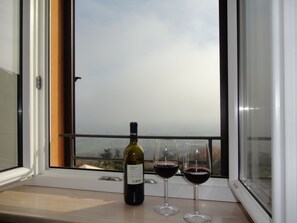 Una botella de vino y dos copas de vino en un alféizar con vistas al cielo y edificios.