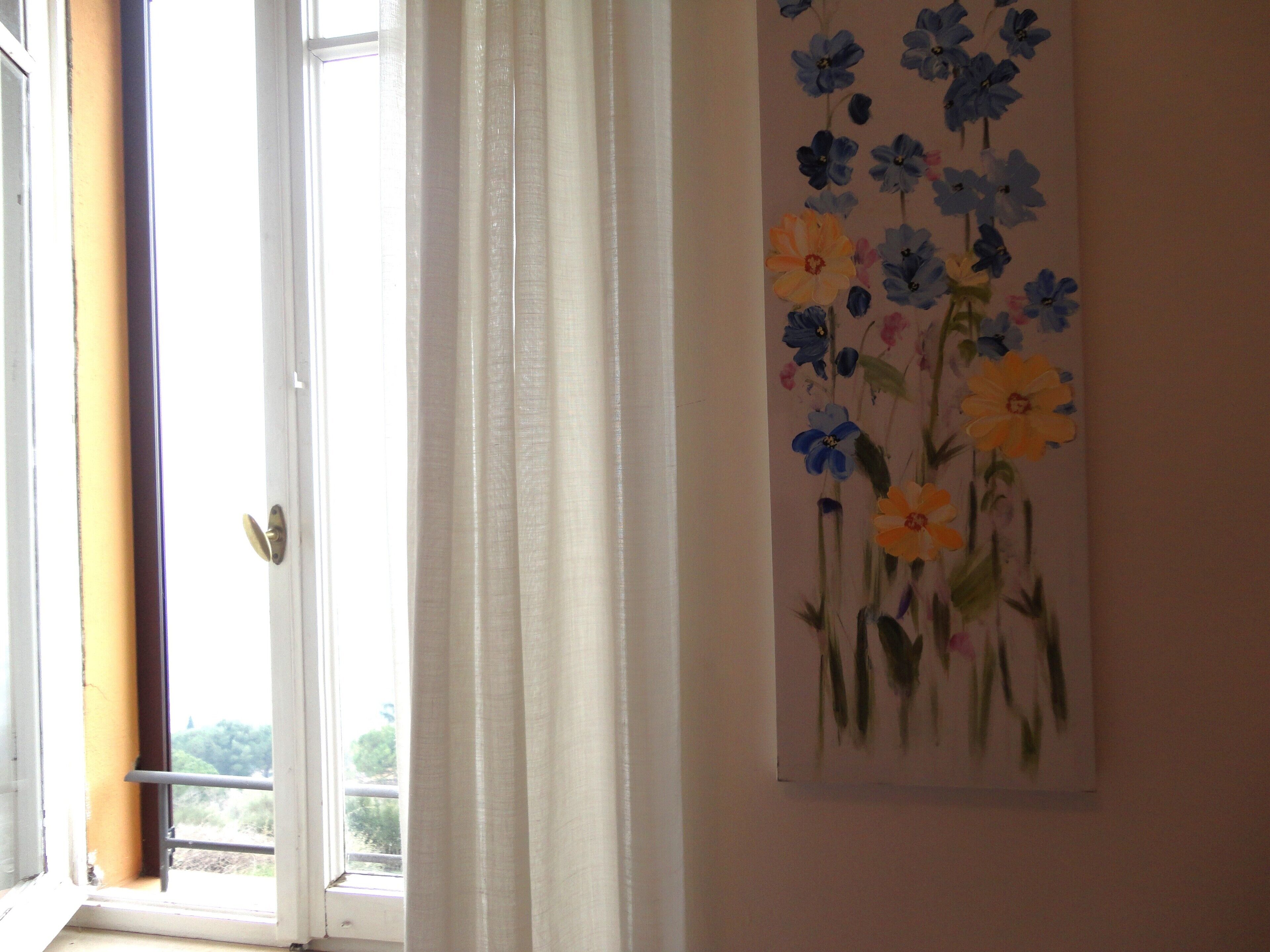 A room with a window, a door, and a floral painting on the wall.