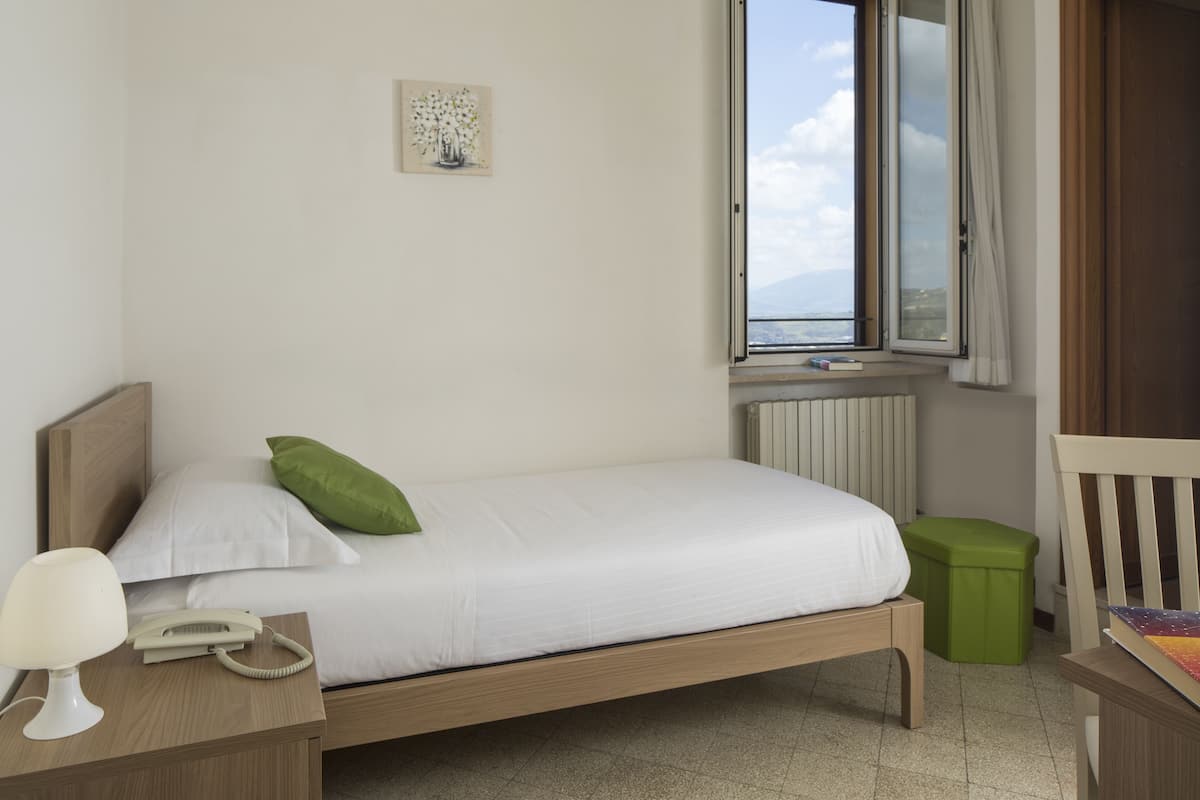 A neatly made bed with a green pillow, a bedside lamp, a telephone, and a green trash bin.