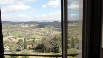 Blick aus einem Fenster auf eine ländliche Landschaft mit Feldern, Bäumen und entfernten Gebäuden.