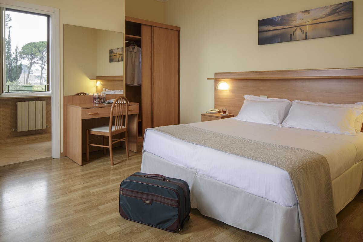 A hotel room with a bed, a desk, a chair, a wardrobe, and a suitcase.
