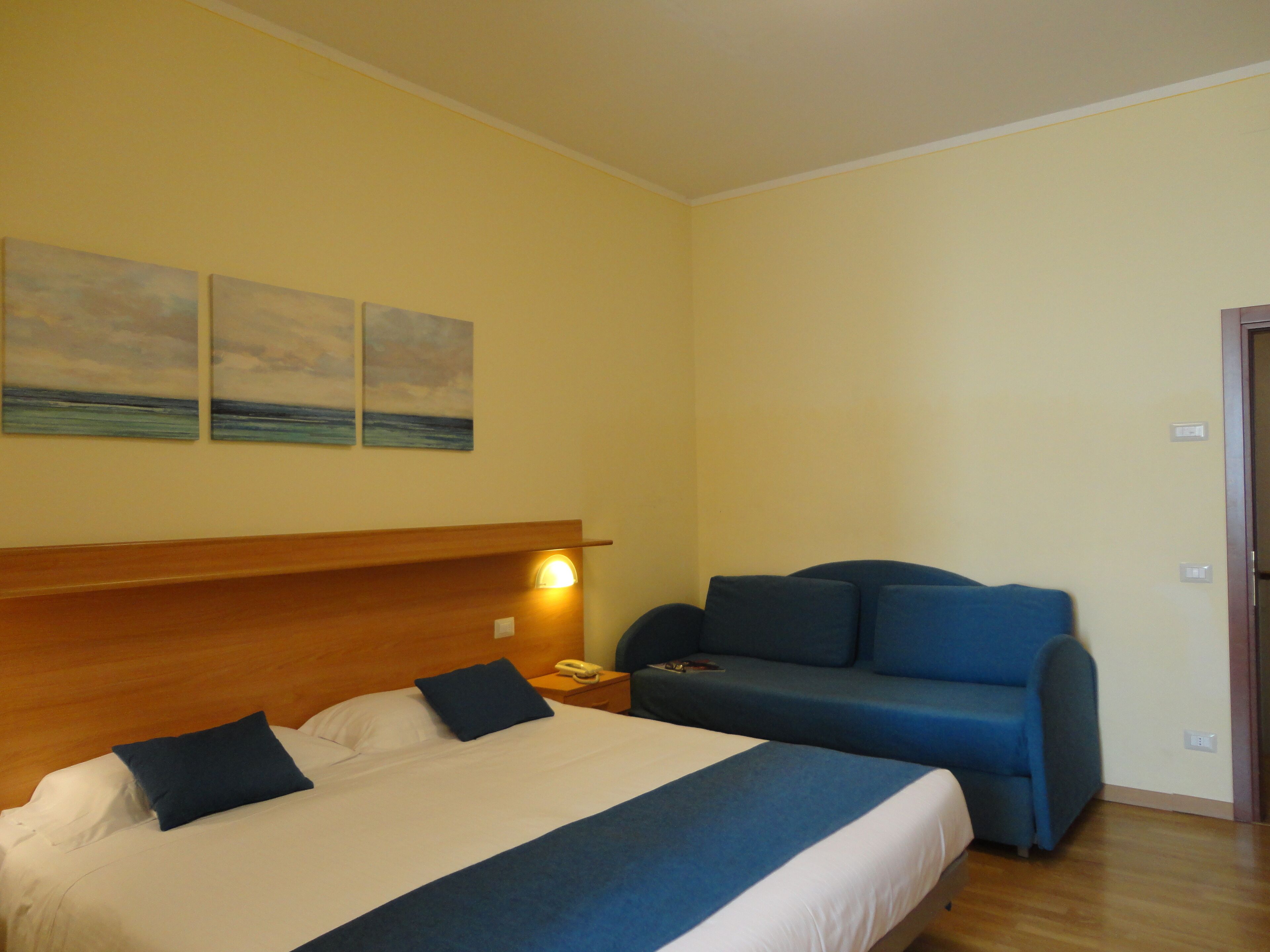 Une chambre d’hôtel avec un lit, un canapé et trois tableaux accrochés au mur.