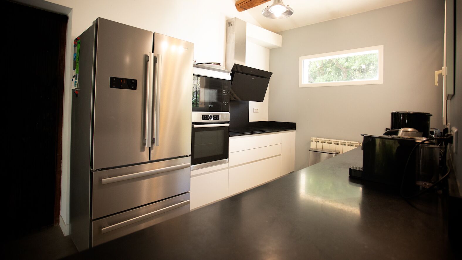 A modern kitchen with stainless steel appliances, white cabinetry, and a large window providing natural light.