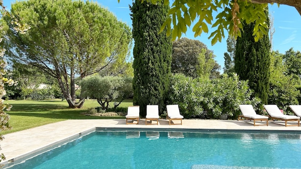 Una piscina azul cristalina con sillas de descanso blancas y un jardín cuidado.