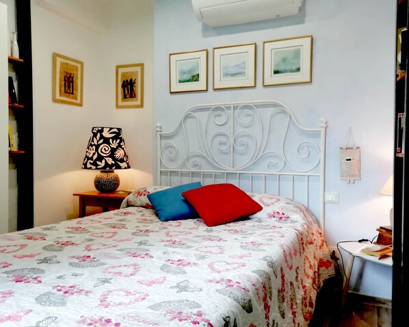 A neatly made bed with floral bedding, a bedside lamp, and a wall with framed pictures.
