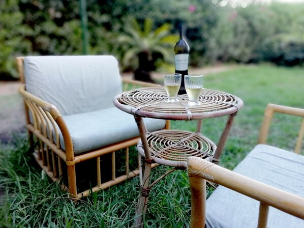 Un conjunto de silla y mesa de mimbre al aire libre, con una botella y vasos sobre la mesa.
