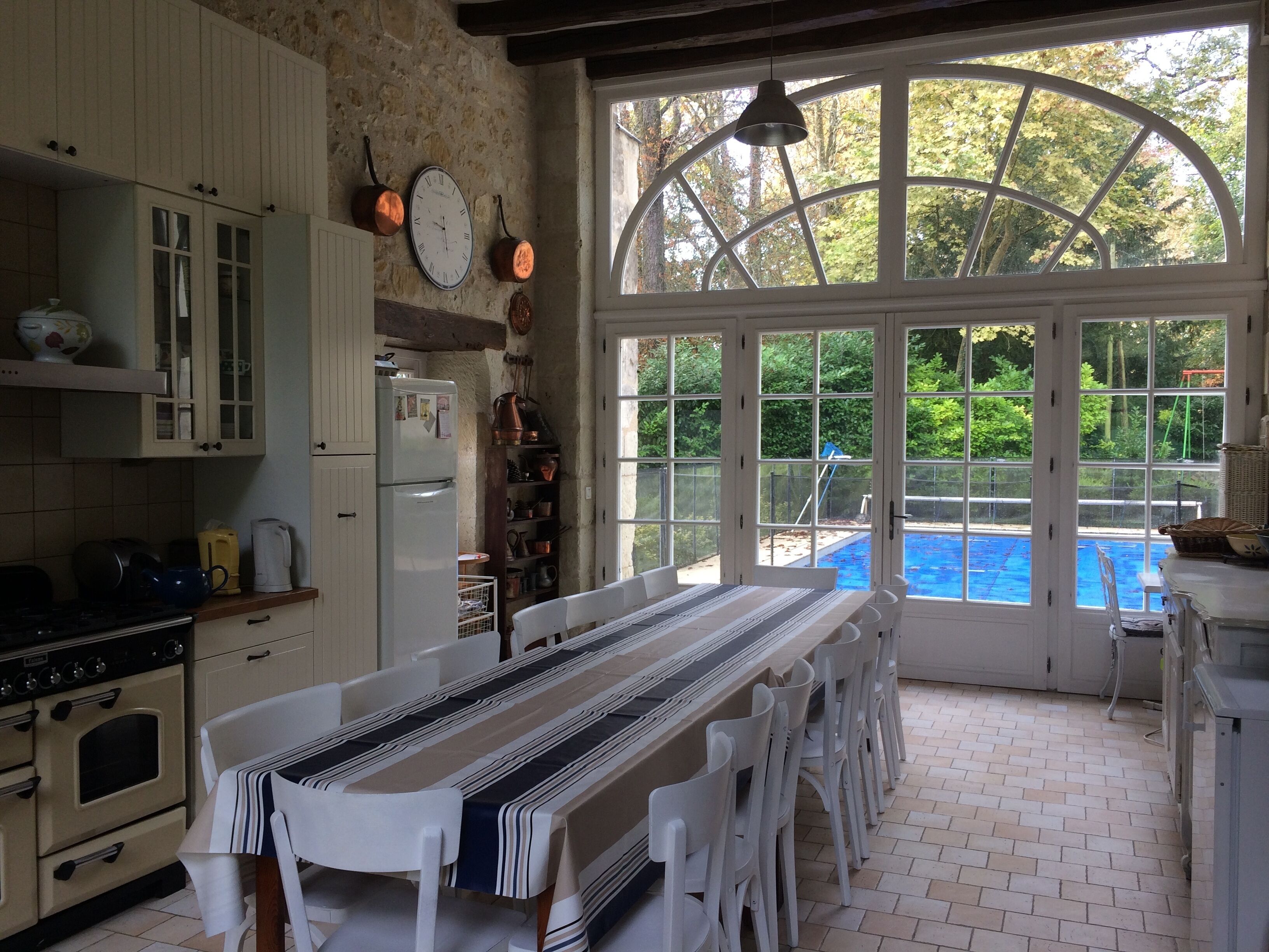 Une cuisine avec une table à manger, des meubles blancs et une vue sur une piscine, visible à travers de grandes fenêtres.