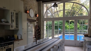 A kitchen with a dining table, white cabinets, and a view of a swimming pool through large windows. - Large family house with pool in the heart of the Loire Valley (Langeais)