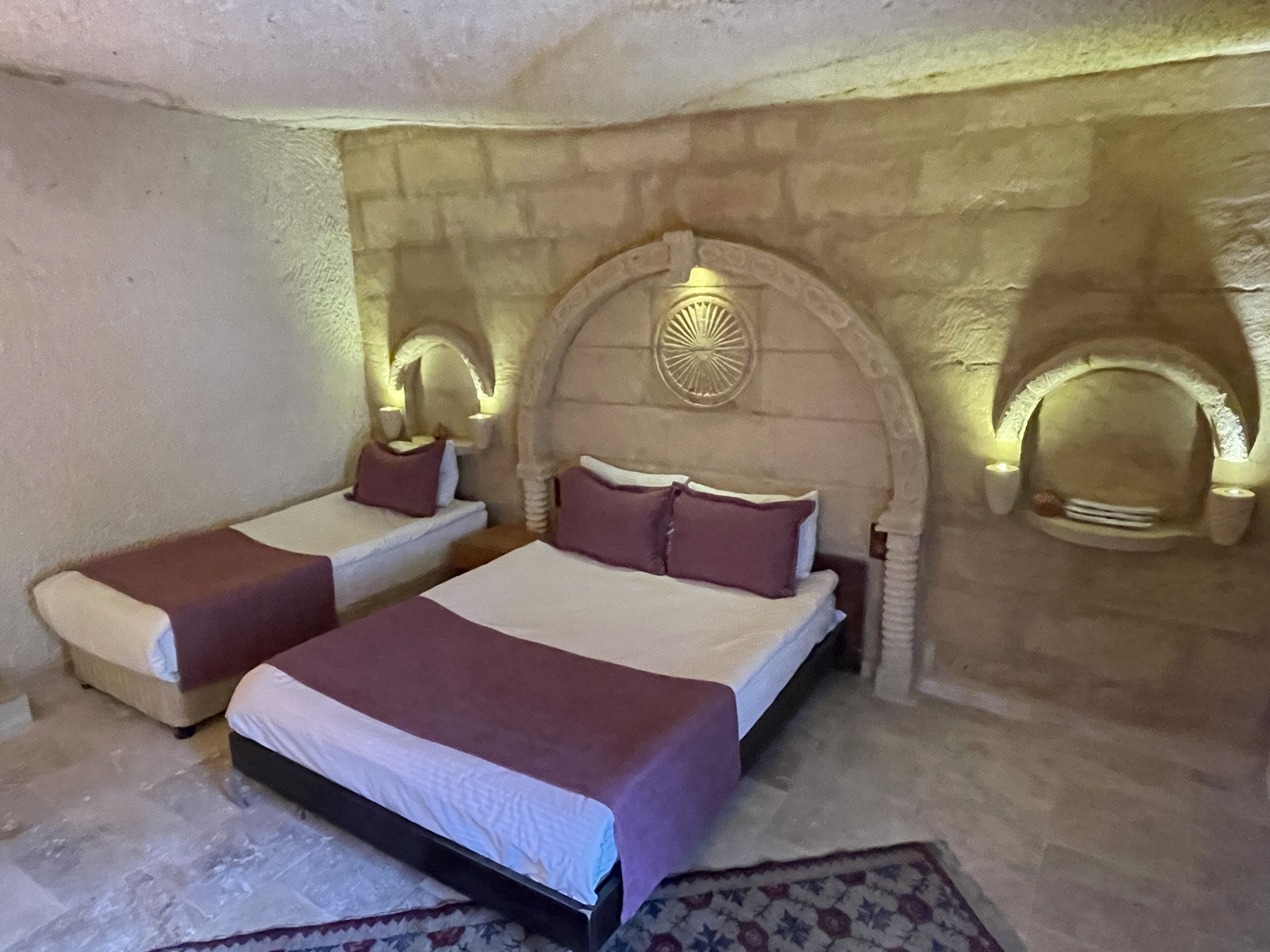 A bedroom with two beds, a stone wall, and a decorative ceiling light fixture.