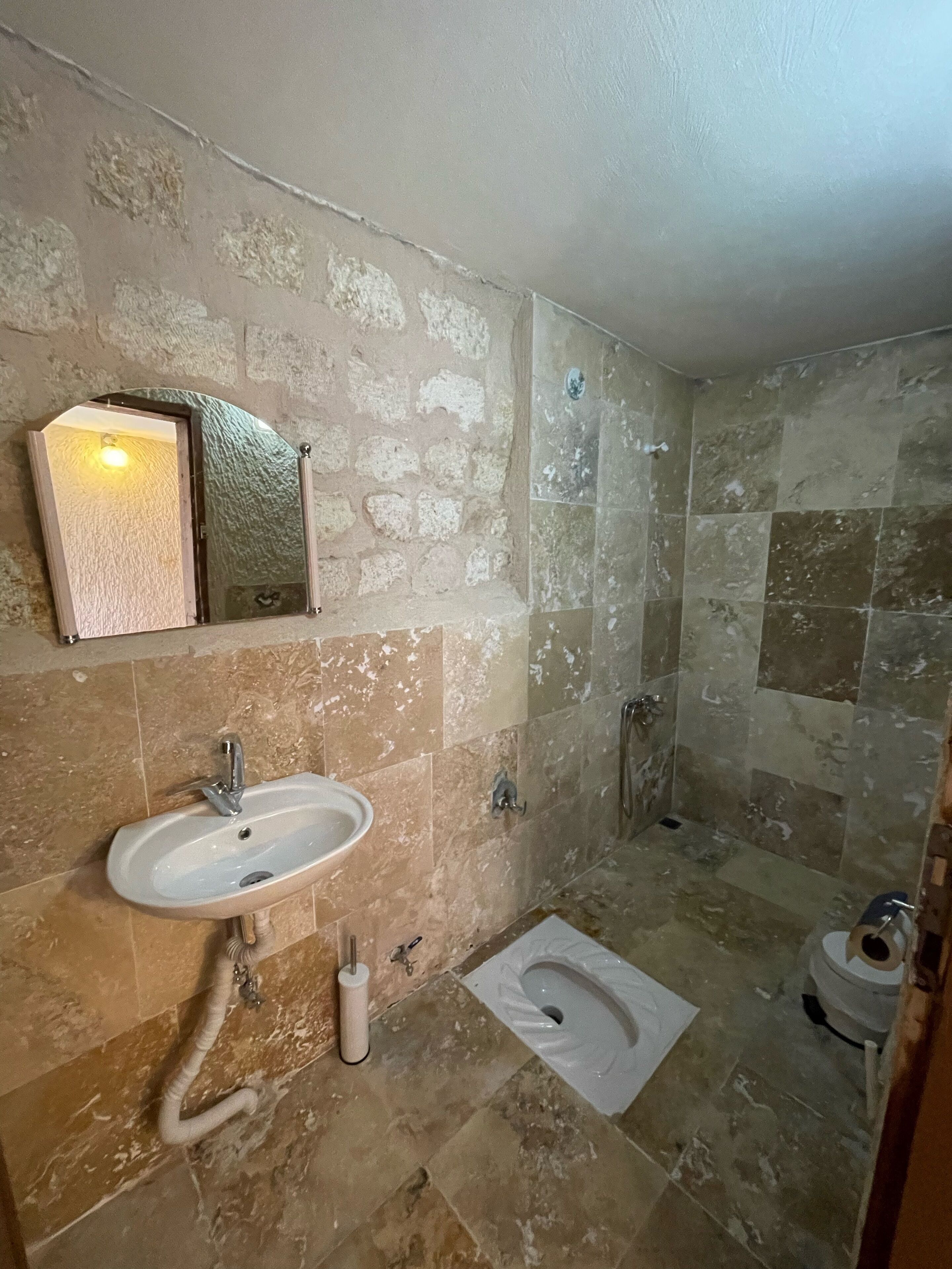 A bathroom with a stone wall, a sink, a mirror, and a shower area.