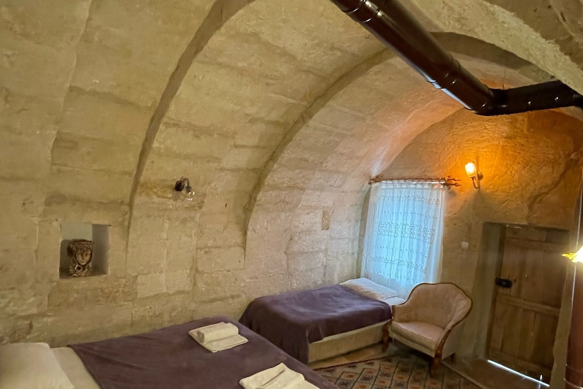 Habitación con dos camas, una silla y una mesita. Tiene paredes de piedra y techo inclinado.