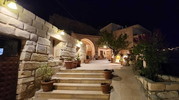 Un edificio de piedra con una escalera que lleva a una puerta, rodeado de macetas con plantas e iluminación exterior.