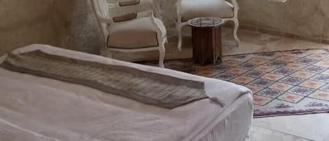 A bedroom with a bed, a chair, a small table, and a window with curtains.