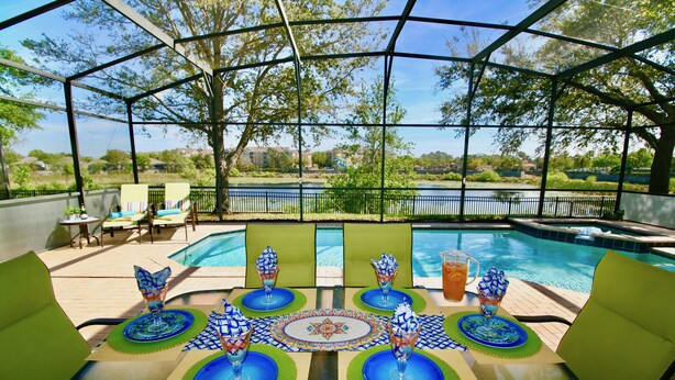Un espace extérieur aménagé, abrité et doté de sièges, offrant une vue sur la piscine, avec une table recouverte de sets de table bleus et verts, et des chaises avec des coussins.