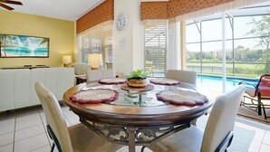 Un coin repas avec une table ronde, des chaises, une horloge et une vue sur une piscine.