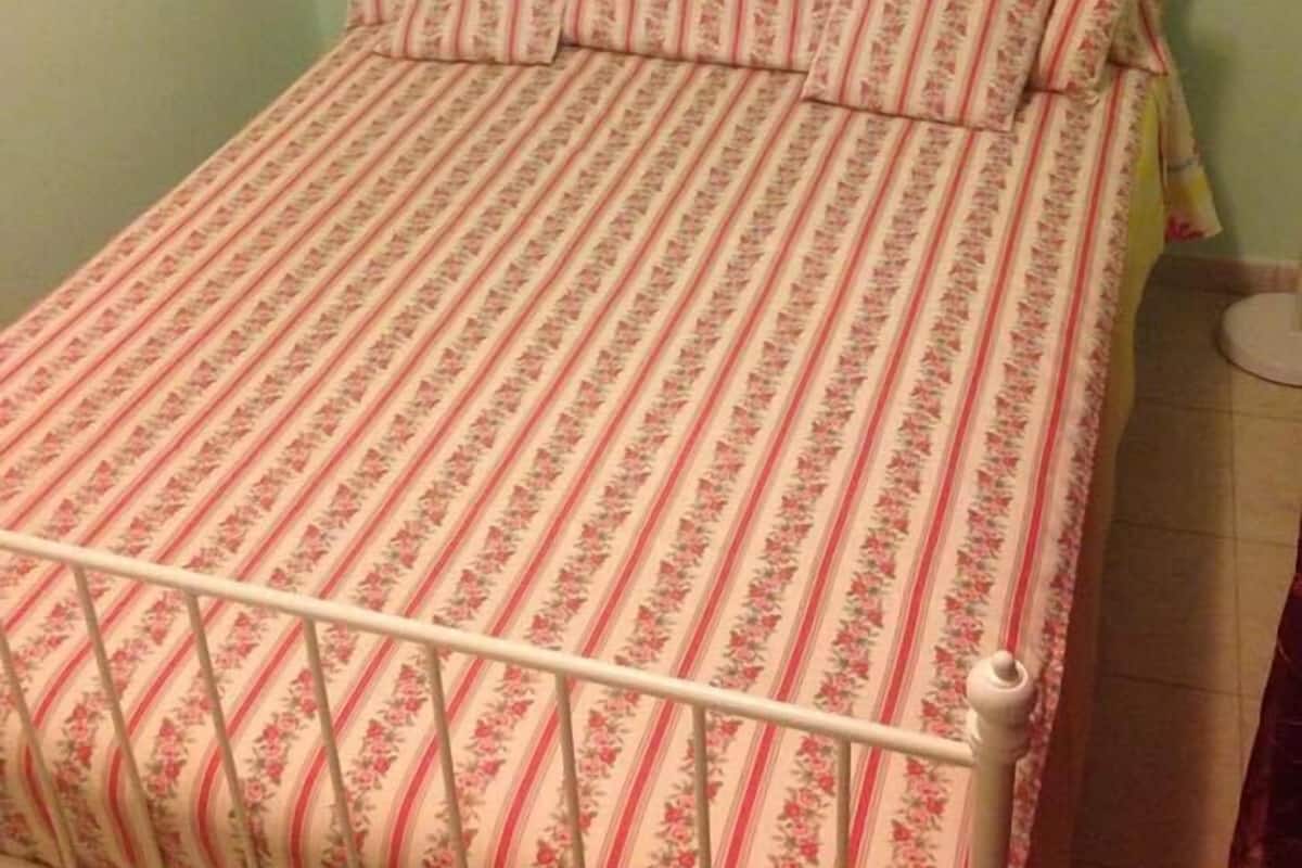 A bed with a floral patterned bedspread and matching pillows, a white metal frame, and a plain wall in the background.