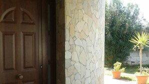 A stone wall with a wooden door, potted plants, and a tiled patio. - Villa La Martina (Syracuse)