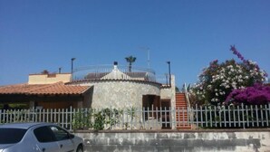 A stone building with a tiled roof, a metal fence, and a staircase leading to a balcony. - Villa La Martina (Syracuse)