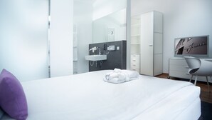 A modern hotel room with a large bed, a bathroom with a sink and mirror, a desk with a chair, and a TV on the wall. - &REPEAT Köln Airport (Cologne)