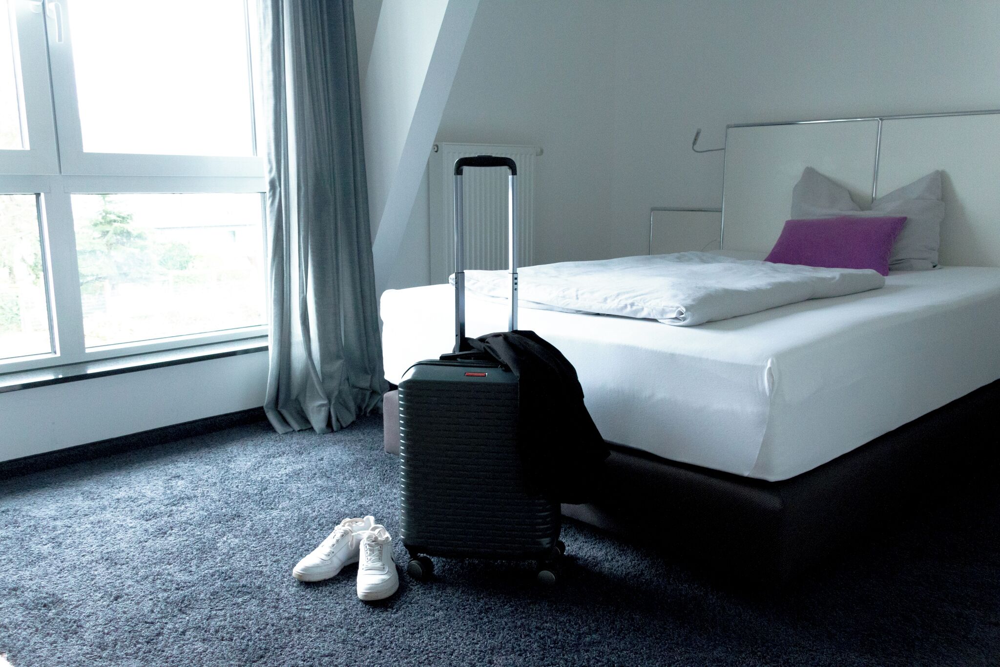 Ein Hotelzimmer mit einem Bett, einem Koffer und einem Paar Schuhe auf dem Boden.