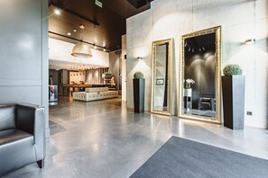A modern lobby with a sofa, a reception desk, and a seating area with chairs. - &REPEAT Köln Airport (Cologne)