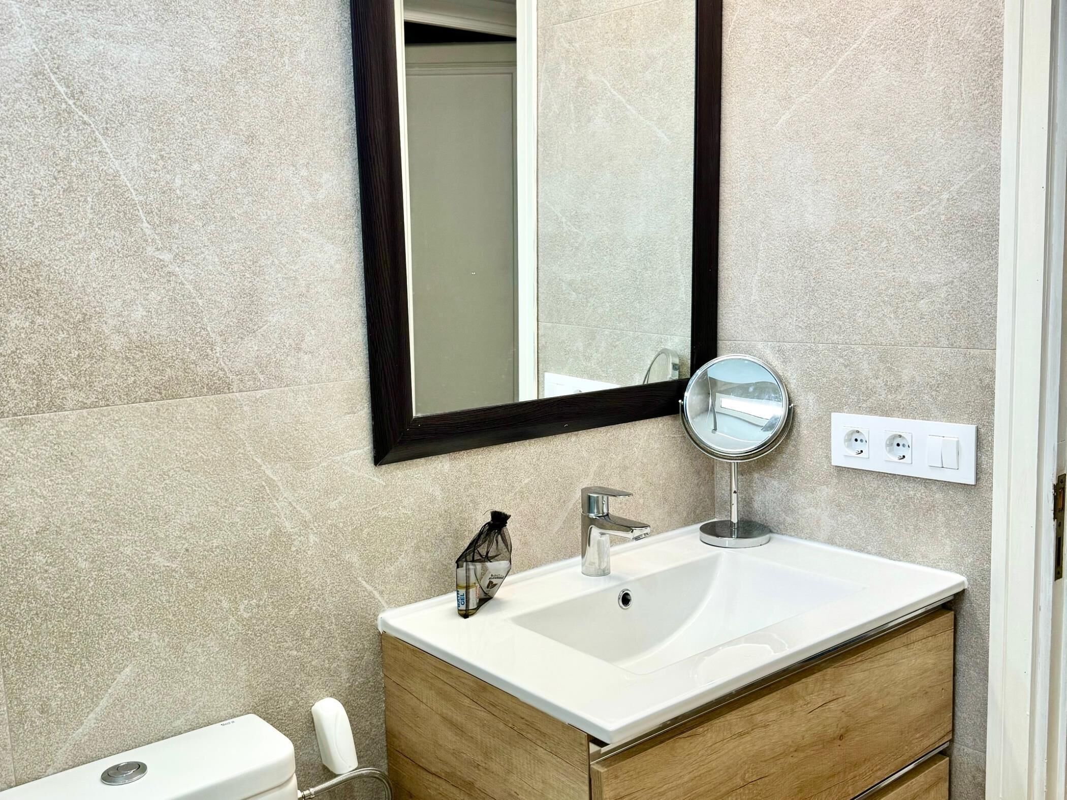 Une salle de bain avec un lavabo blanc, un meuble-lavabo en bois, un miroir et des toilettes.