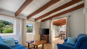 A spacious living room with a wooden ceiling, a television, a dining area, and a view of greenery outside. - Villa Roser Vell By SunVillas Mallorca (Pollença)