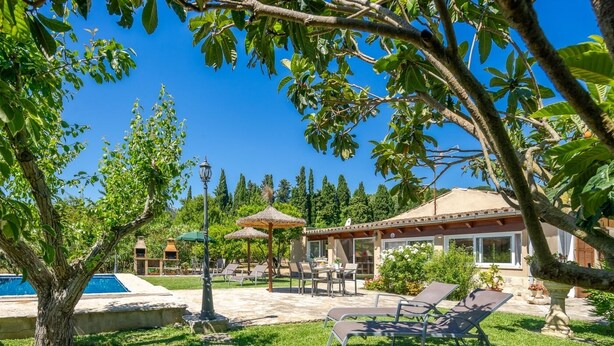 A poolside area with lounge chairs, a pergola, and a house with a tiled roof. - Villa Roser Vell By SunVillas Mallorca (Pollença)