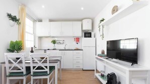 Eine moderne Küche mit weißen Schränken, einer Essecke mit Tisch und Stühlen, einer Mikrowelle, einem Kühlschrank und einem Fernseher auf einem weißen Schrank.