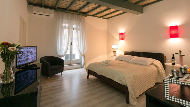A hotel room with a bed, a TV, a chair, a desk, and a vase with flowers.